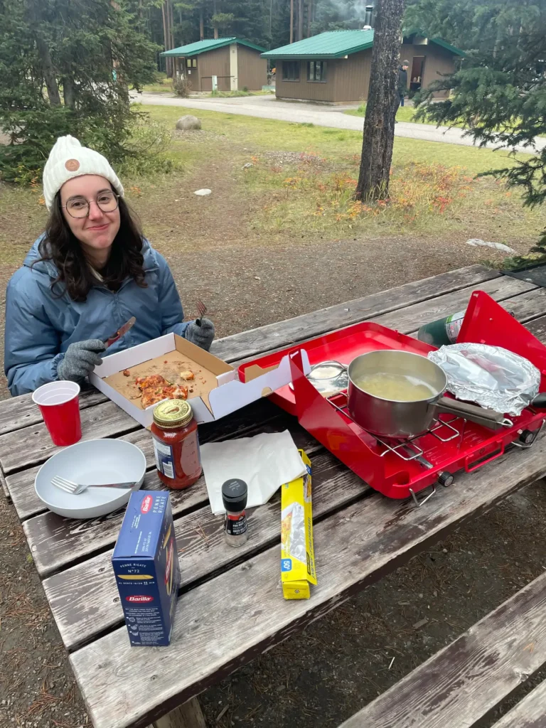 Gwen, portant doudoune et gants, attablée à une table de pique nique en train de manger une pizza