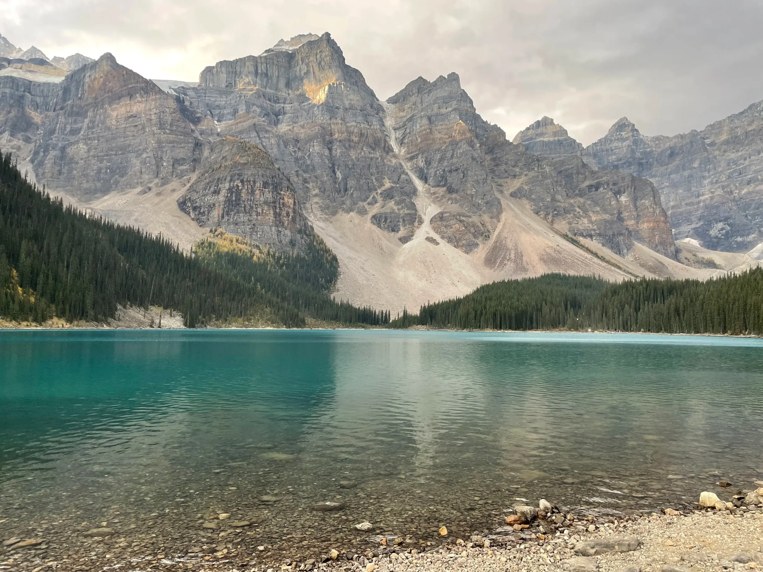 Lac turquoise entourée de montagnes sous un temps nuageux