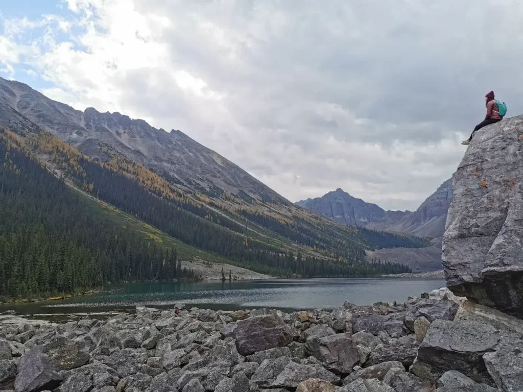 Des rochers sont au premier plan avec un plus gros rocher sur la droite de la photo où l'on peut voir une personne assise dessus.