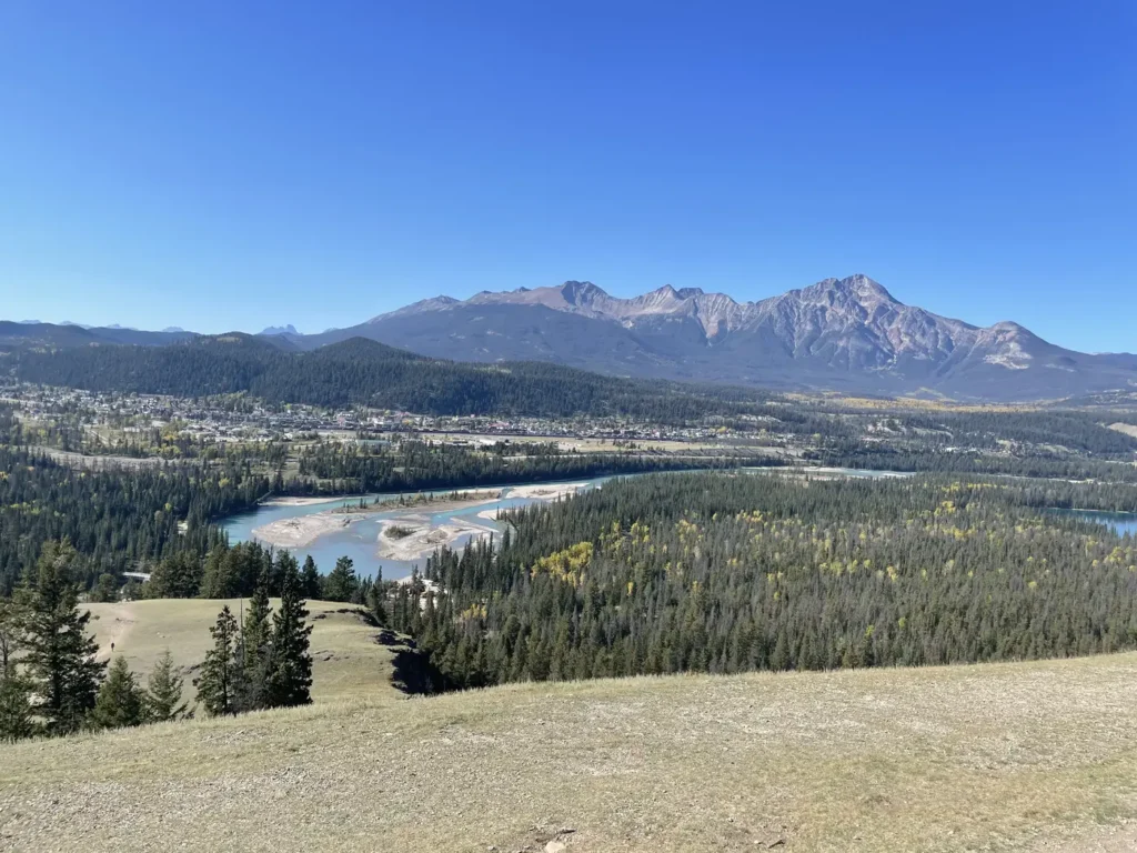 Vue panoramique sur la rivière Athabasca qui a une couleur bleu très glacial. En arrière plan, on peut apercevoir la ville de Jasper ainsi qu'une montagne.