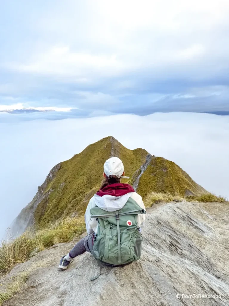 Gwen assise sur un rocher admirant les nuages qui sont en-dessous d'elle