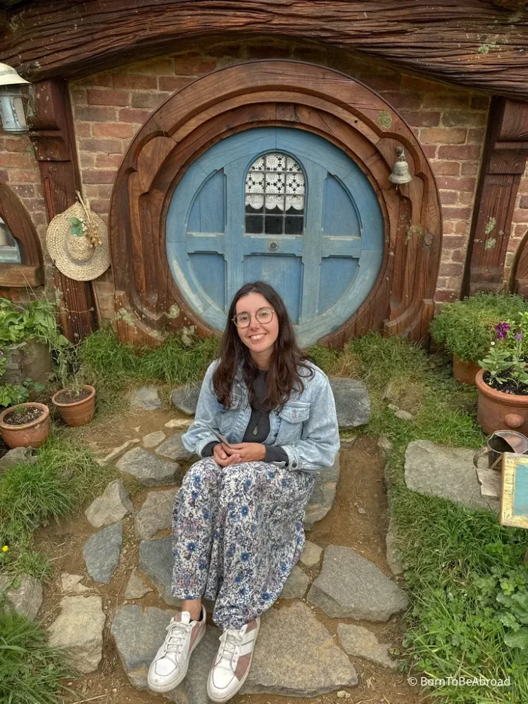 Gwen face à une toute petite porte d'une maison de Hobbit