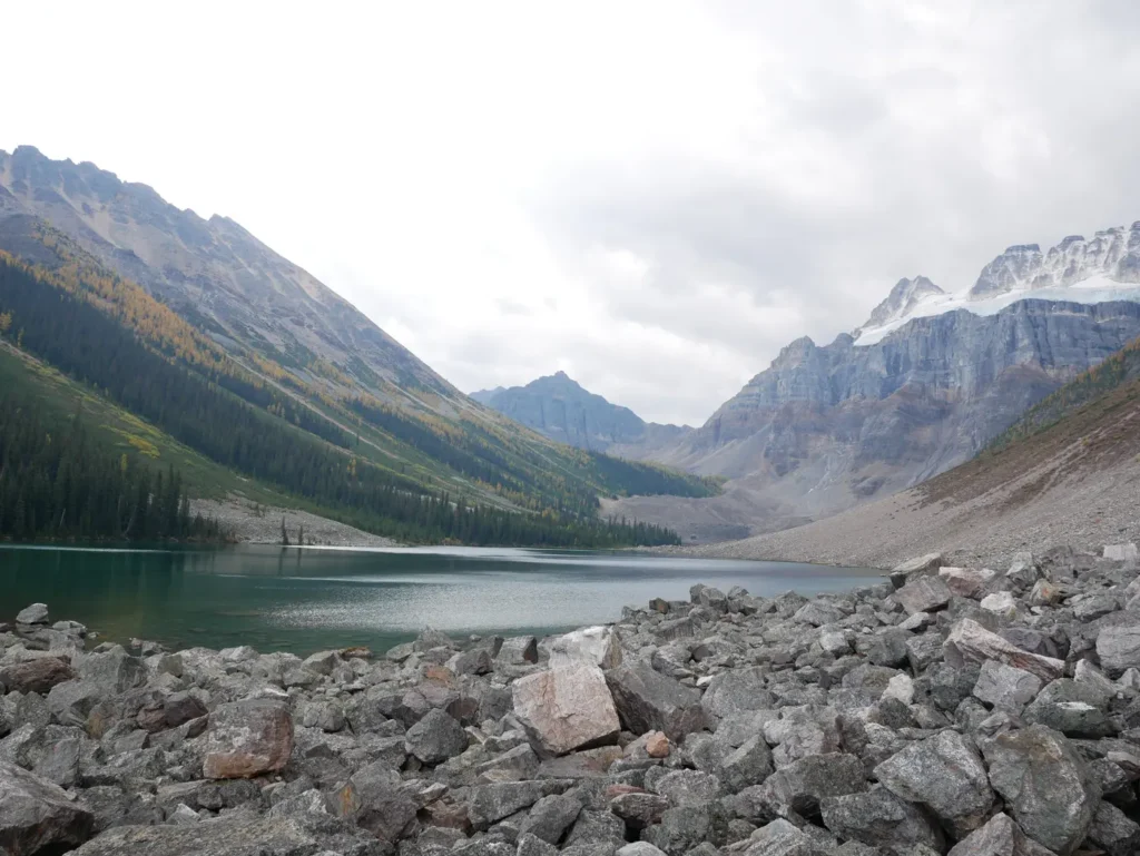 Rochers en premier plan. Lac en second plan entouré de montagnes. Le temps est nuageux